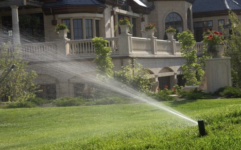 Regner bewässert Garten vor Haus